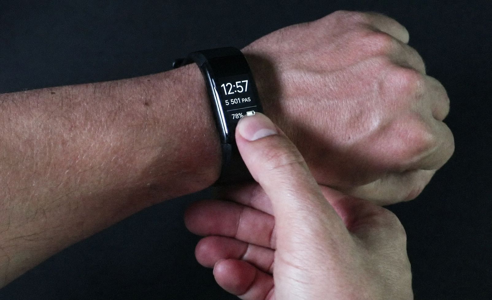 Montre connectée noire portée au poignet affichant l'heure, le nombre de pas et la batterie